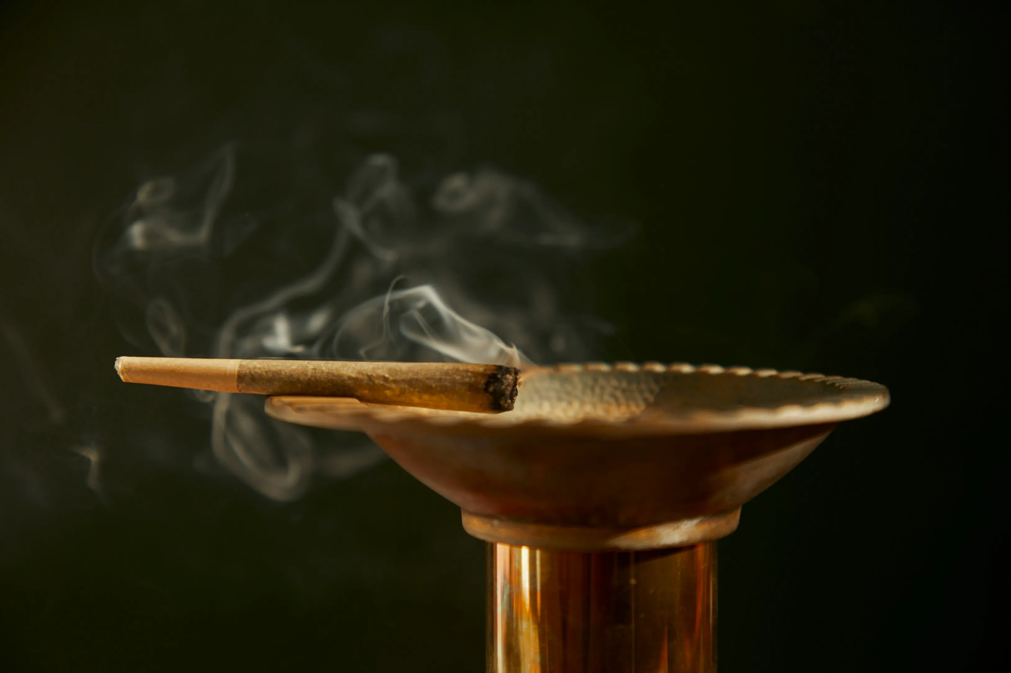 A lit joint resting on a ceramic ashtray with smoke curling upward  -  a ritual older than prohibition