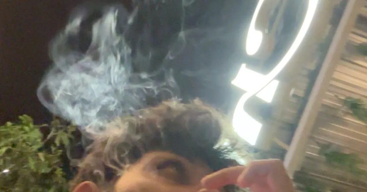 Close up of smoke drifting past a glowing neon sign at night, a mood shot for cannabis content