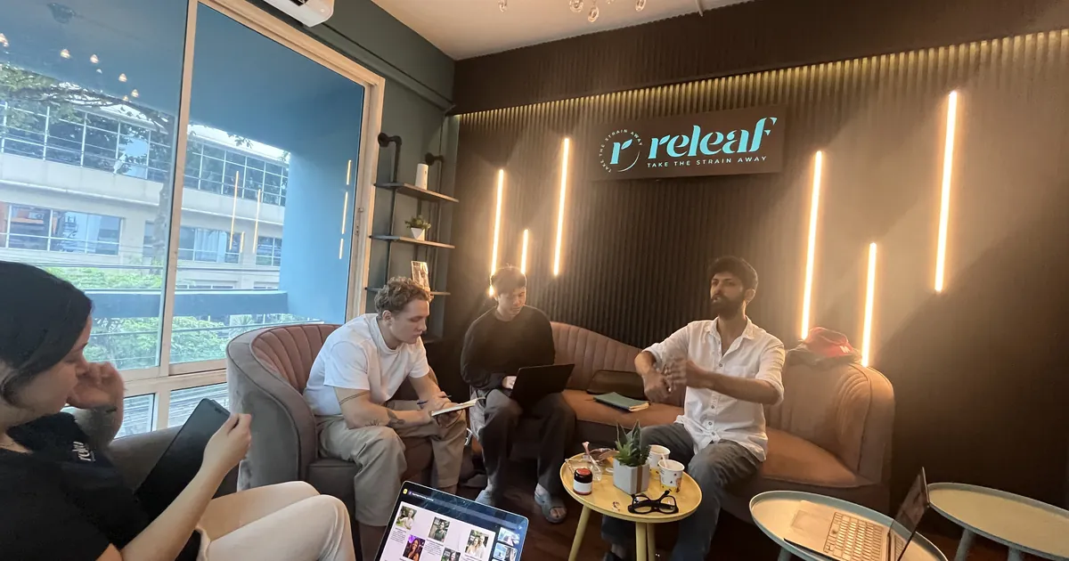 People talking and working on lounge chairs in a dispensary with a releaf sign glowing on the wall