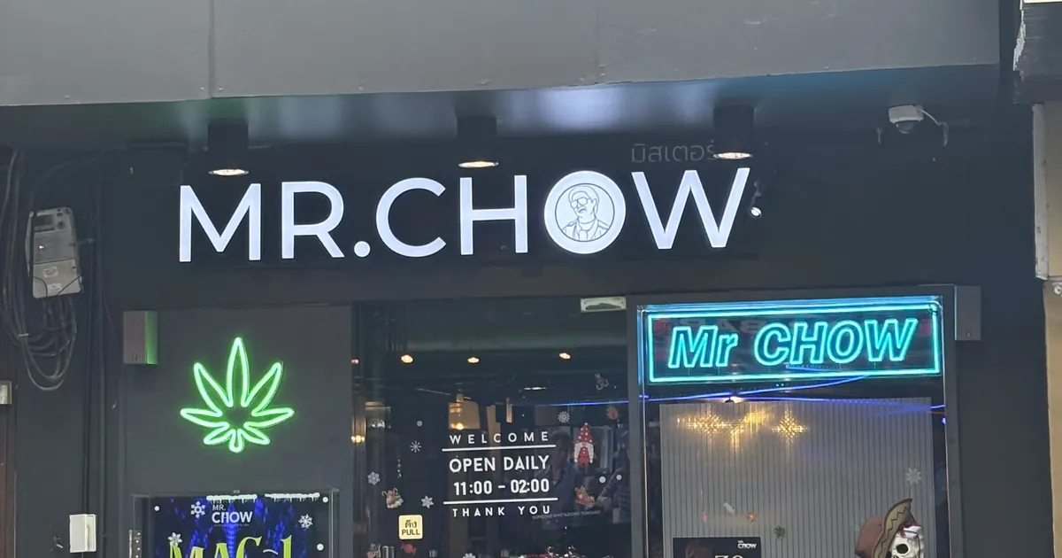 Shopfront at night with a Mr Chow sign, a green neon cannabis leaf and opening hours on the glass door