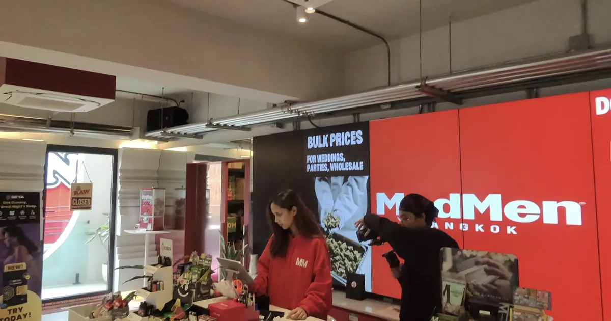 Shop interior with a large red MedMen Bangkok screen and two staff working at a counter