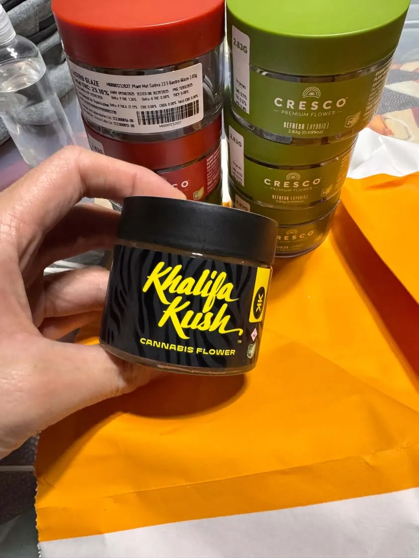Hand holding Khalifa Kush branded cannabis jar with other jars in background