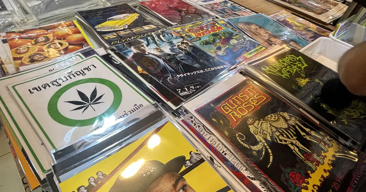 Posters and prints laid out for sale, including a green cannabis leaf sign with Thai text