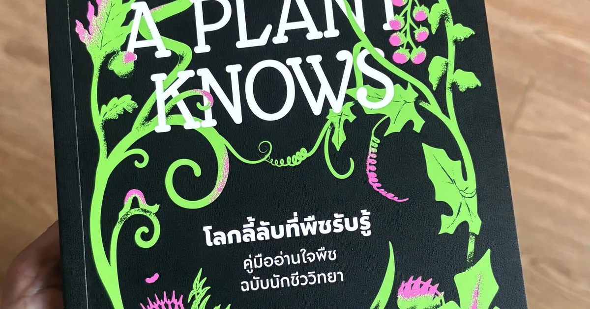 Hand holding a dark green book titled A Plant Knows, with leafy vines and Thai text on the cover