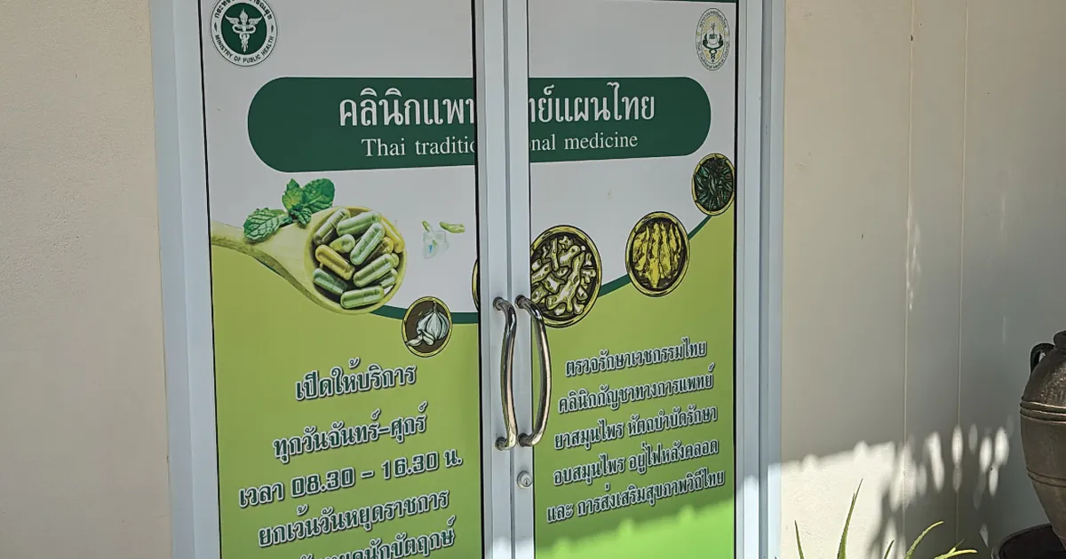 Glass door with a green traditional medicine clinic sign in Thai and English showing herbs and capsules