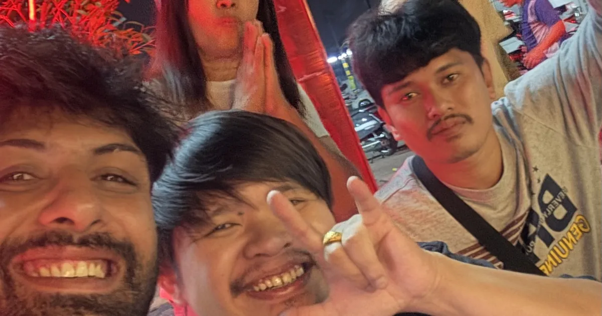 Three friends crowd into a night time selfie, smiling, with red lights behind them